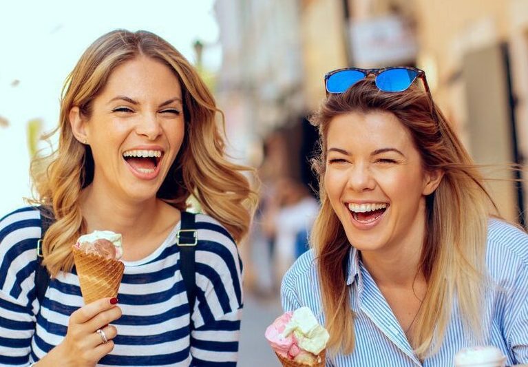 Two young women laughing and holding ice cream in hand