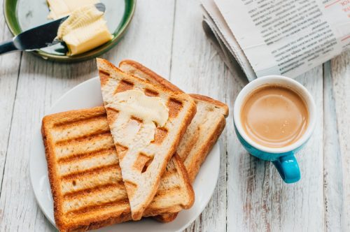 Breakfast with coffee, toasts, butter and jam on white wooden background