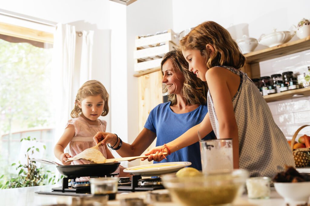Little sisters cooking with her mother in the kitchen.